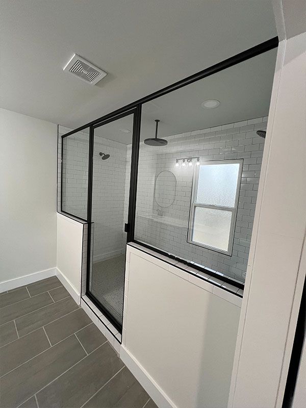 Modern bathroom with glass shower enclosure, white tile walls, and gray floor tiles.