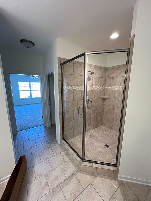 Empty tiled hallway with a glass shower enclosure and a bright room in the background
