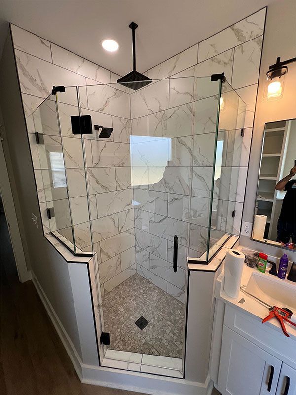 Walk-in shower with marble-look tile, black fixtures, and a glass door in a bathroom