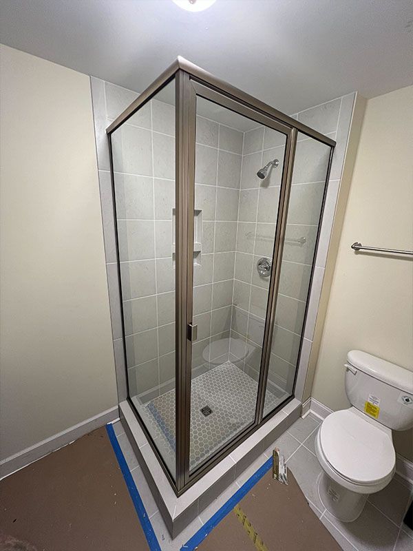 Corner shower with glass doors in a small bathroom next to a toilet, with blue tape on the floor edges.