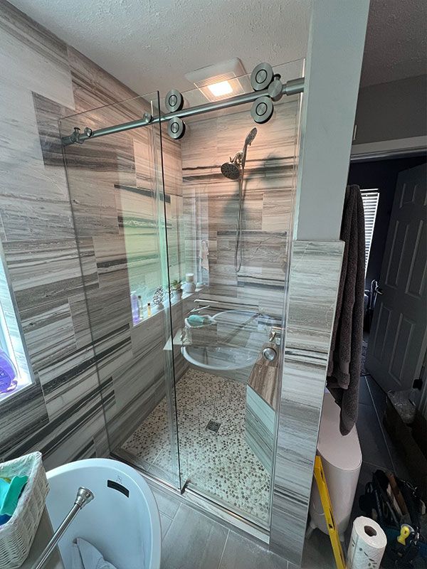 Small tiled bathroom with glass shower enclosure, sink, mirror, and a laundry basket in the foreground