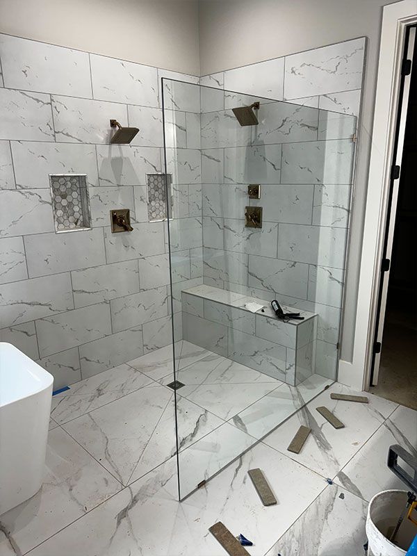 Modern tiled bathroom with glass shower enclosure and built-in bench, white marble-look walls and floor.
