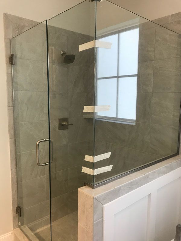 Glass shower enclosure with gray tile and a window beside a white bathtub