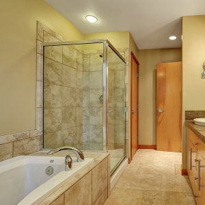 Modern bathroom with glass-enclosed shower, bathtub, beige tile, and vanity.