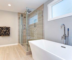 Modern bathroom with glass shower, freestanding tub, light wood floor, and frosted window