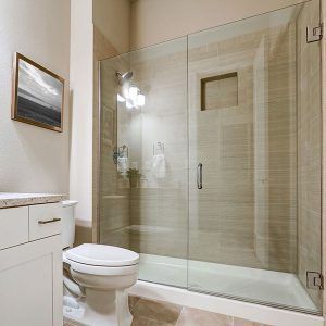 Modern bathroom with glass shower, toilet, and white vanity against beige walls