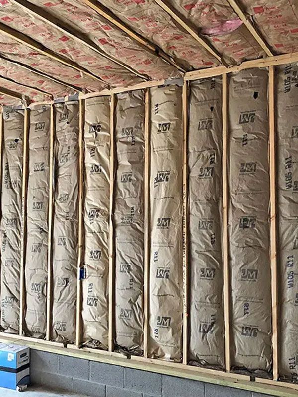 Unfinished wall with exposed insulation between wooden studs and roof rafters