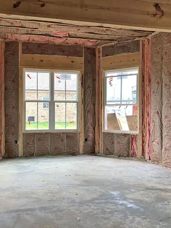 Unfinished room with exposed pink insulation, rough walls, and two windows letting in daylight