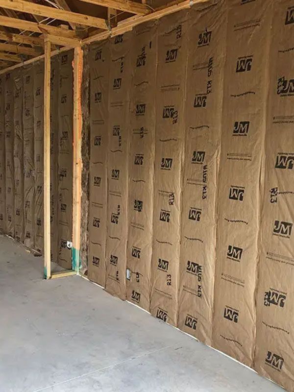 Unfinished interior wall with exposed wood framing, insulation wrap, and concrete floor under construction