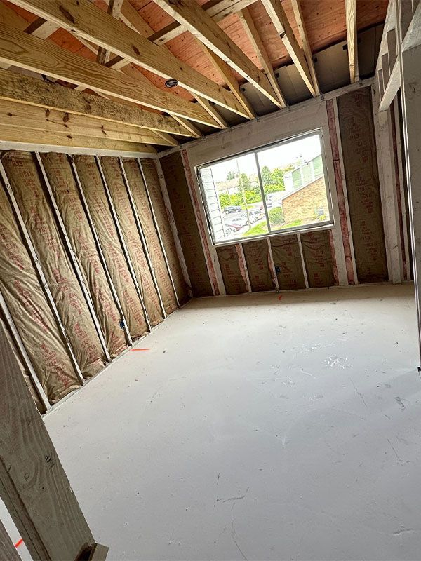 Empty unfinished room with exposed wood framing, slanted ceiling, and a large window opening.