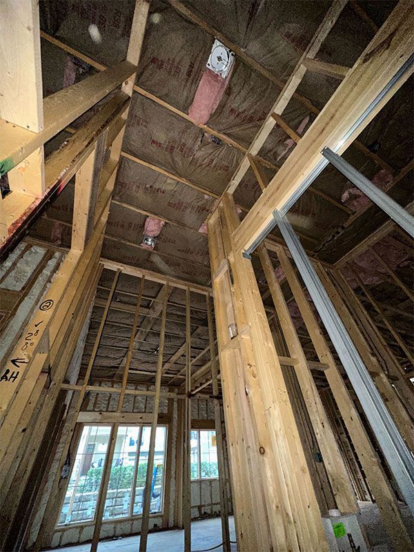 Interior framing of a house under construction, with exposed wooden studs and ceiling beams.