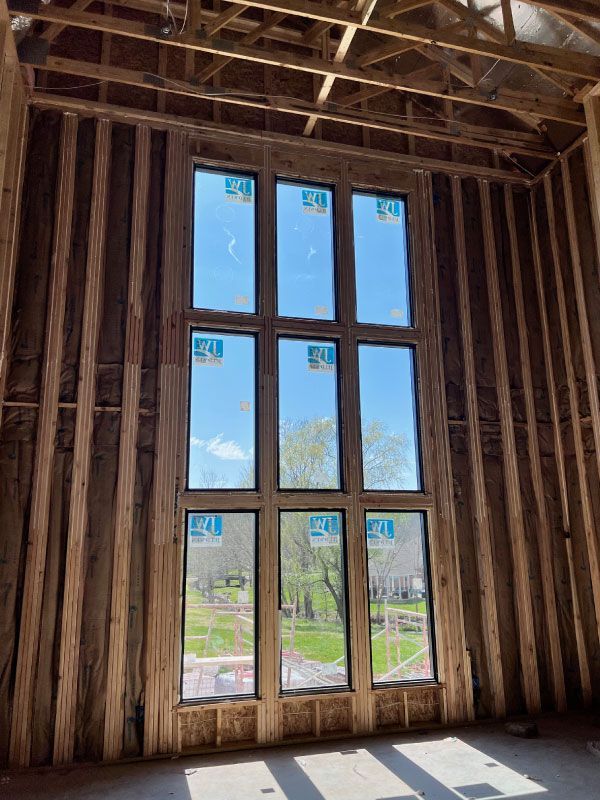Unfinished room with exposed wooden framing and a tall window grid overlooking blue sky and trees
