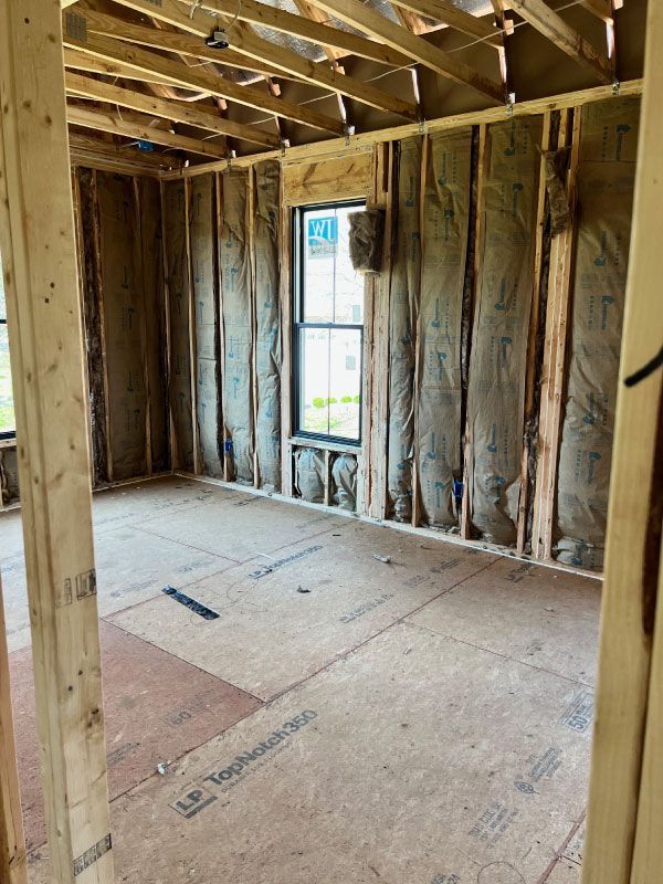 Unfinished room with exposed wood framing, insulation, plywood floor, and a single narrow window.