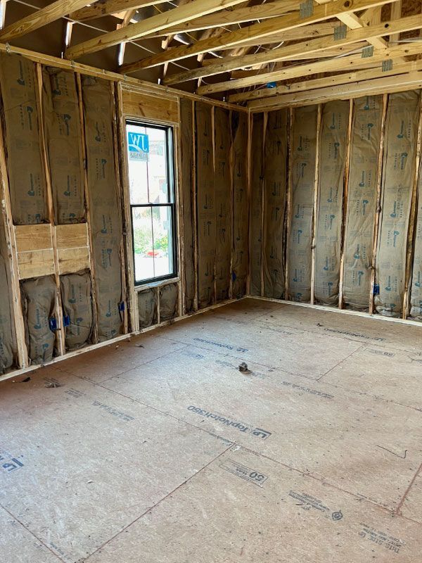 Empty unfinished room with exposed wood framing, insulation, and a single window.