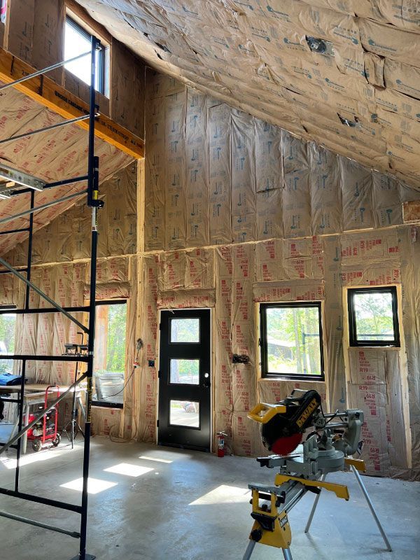 Unfinished interior with high ceiling, exposed insulation, windows, and tools on a concrete floor