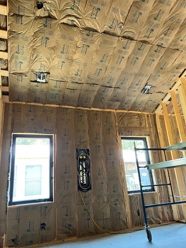Interior room under construction with insulation on walls and ceiling, two windows, and metal framing visible.