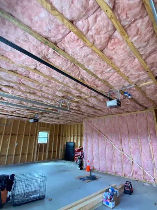 Unfinished insulated attic with exposed framing, pink insulation, and construction tools on the floor.
