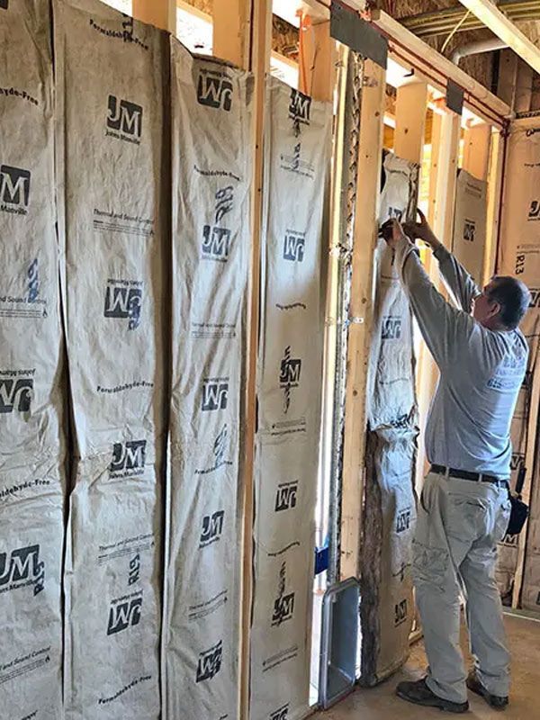 Worker installing insulation batts between wall studs in an unfinished room
