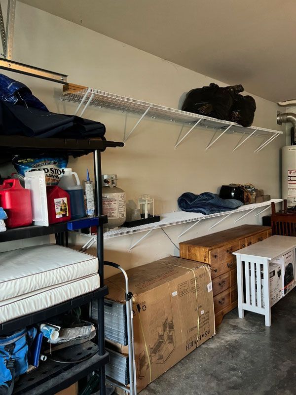 Garage storage shelves with tools, bins, folded fabrics, and cardboard boxes along a wall