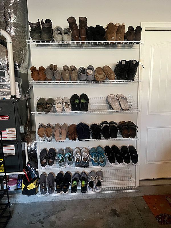 Shoe rack filled with many pairs of shoes in a garage beside a closed white door.