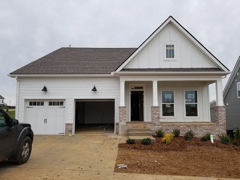 New white suburban house with a two-car garage, tan stone accents, and a gravel driveway
