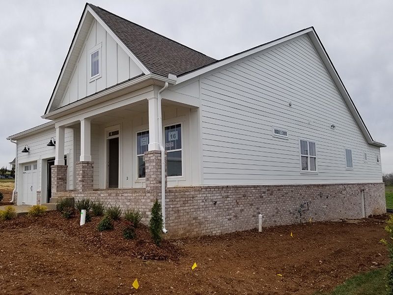New white house with gray roof, brick foundation, and front porch on a dirt lot