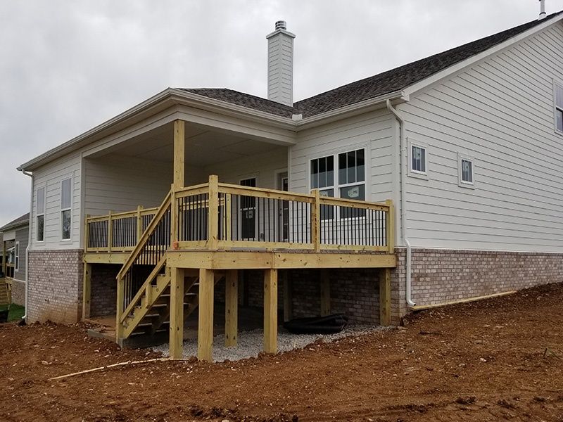 Back porch deck under construction on a white house with unfinished stairs and railing