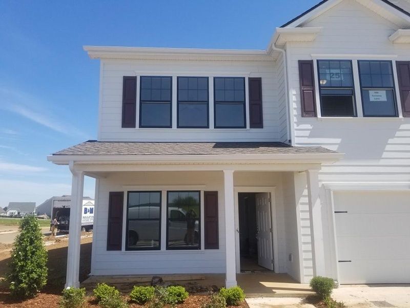 Two-story white suburban house with dark shutters, front porch, and attached garage under a blue sky