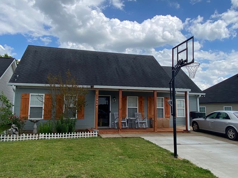 Suburban house with a basketball hoop, driveway, parked car, and partly cloudy sky.