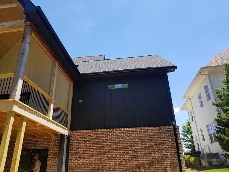 Modern house exterior with dark siding, brick lower wall, and adjacent yellow construction scaffolding