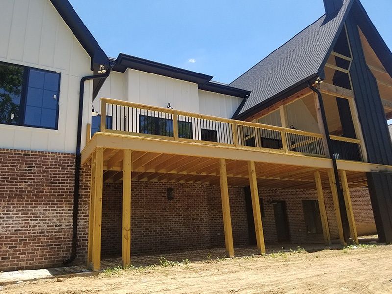 Two-story house with wooden deck and tall support posts over a brick wall under a blue sky