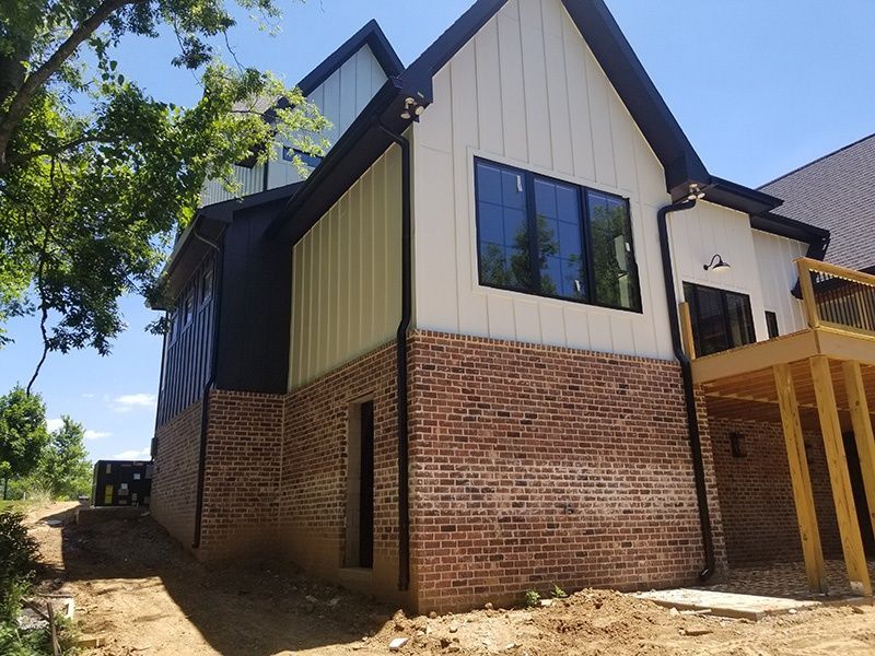 Brick-and-cream two-story house exterior with black roof and large windows, viewed from the side.