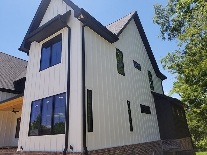 Modern white house exterior with black trim, tall gabled roof, and large windows under a blue sky