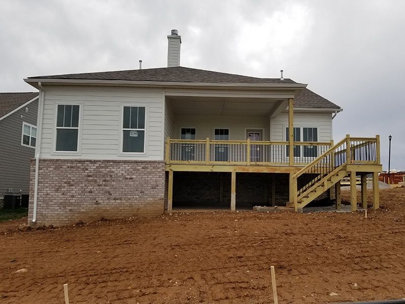 Back view of a raised white house with a brick foundation, porch, and stairs on a dirt lot