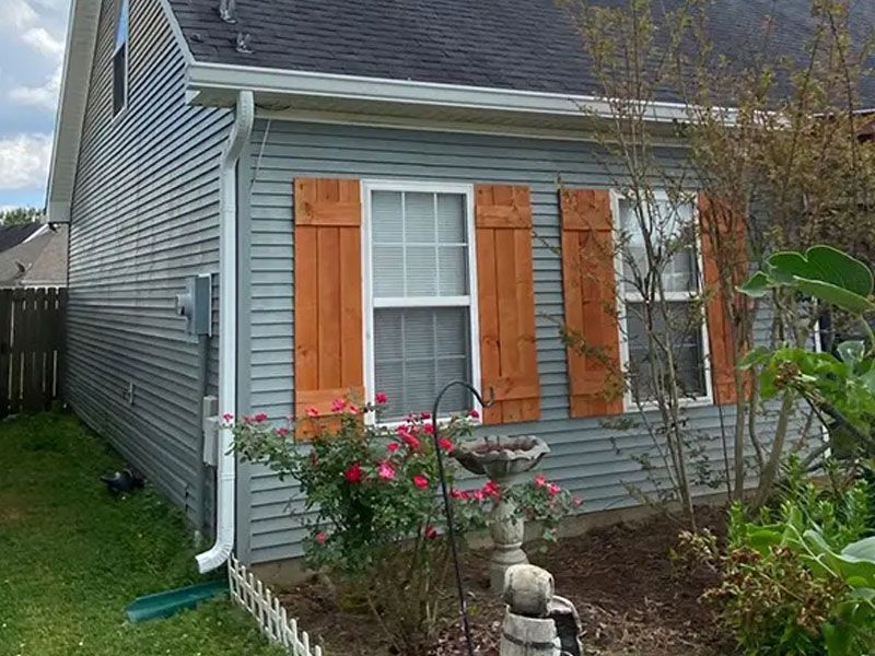 Gray house exterior with orange shutters, white windows, and a small flower garden in front