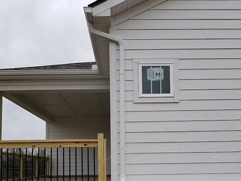 Exterior of a white house with a small window and covered porch railing under an overcast sky