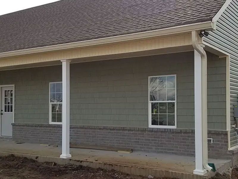 Front of a house with gray siding, white trim, and two white columns on a covered porch.