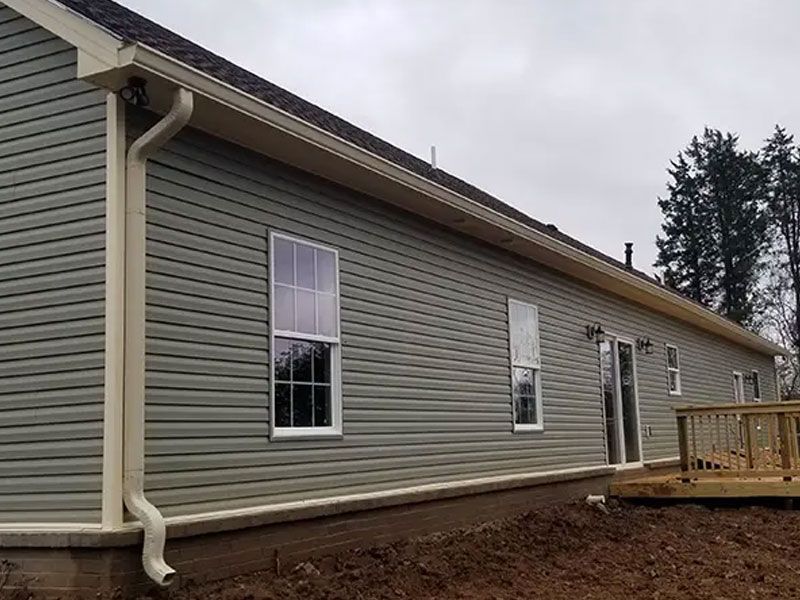 Side view of a gray house with vinyl siding, windows, downspout, and a small wooden deck.