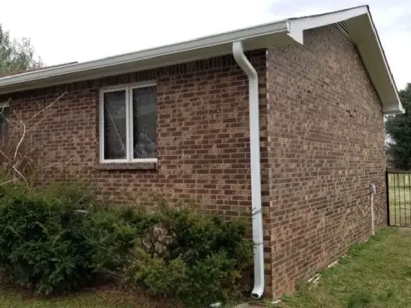 Brick house exterior with a window, white gutter, and shrubs along the wall