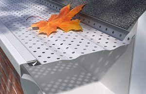 Orange leaf on perforated white metal gutter guard with gray roof shingles nearby