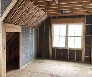 Unfinished attic room with exposed framing, sloped ceiling, and a large window.