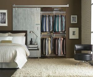 Modern bedroom with open closet, sliding barn door, bed, and black chair on shag rug.