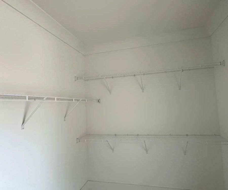 White closet with empty wall-mounted shelves and hanging rods in a bright corner room