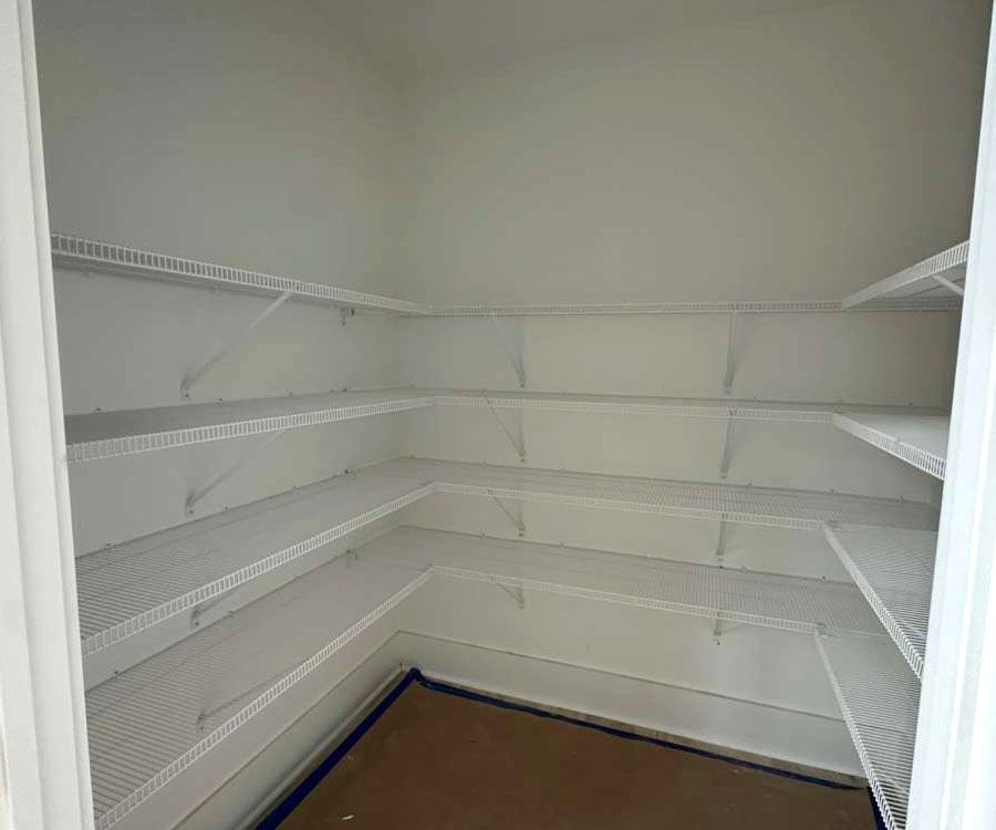Empty walk-in closet with white wire shelves and brown floor.