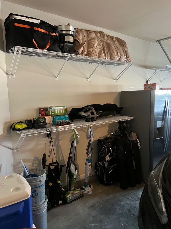 Garage storage area with shelves, tools, bags, and a cooler beside a car.
