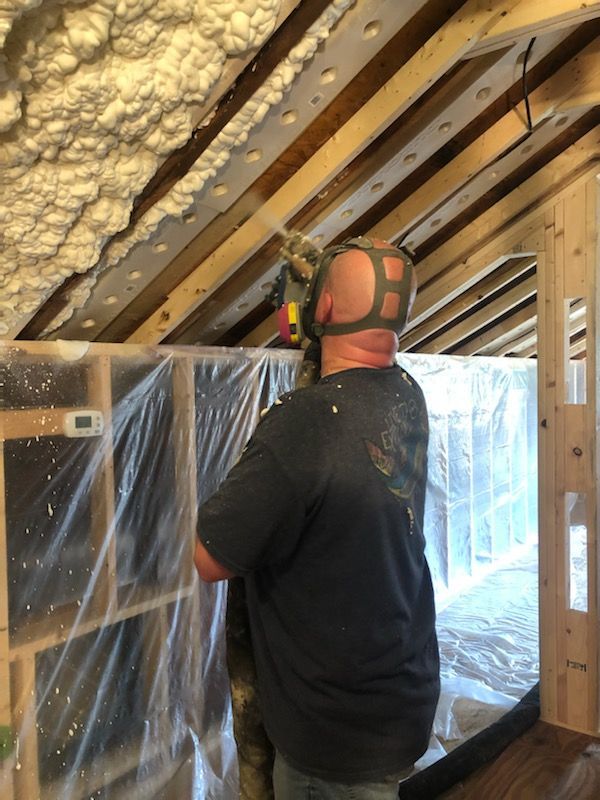 Worker installing insulation in an attic with exposed beams and plastic sheeting
