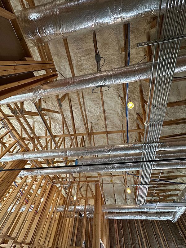 Exposed wooden ceiling framing with metal ducts, pipes, and wiring in an unfinished attic space
