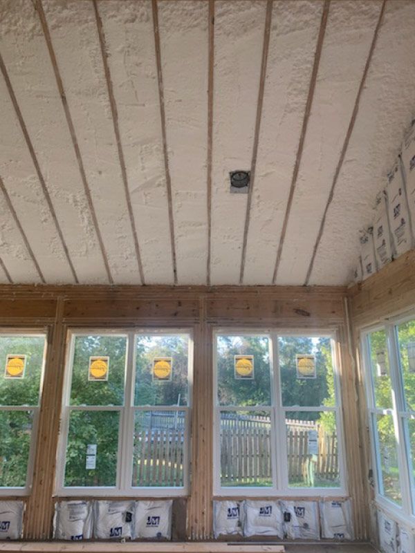 Unfinished sunroom with large windows, exposed insulation, and a small ceiling light.
