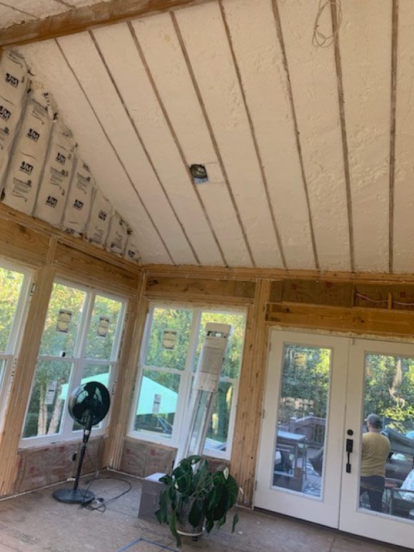 Sunroom interior with unfinished ceiling, glass doors, and two fans near potted plants