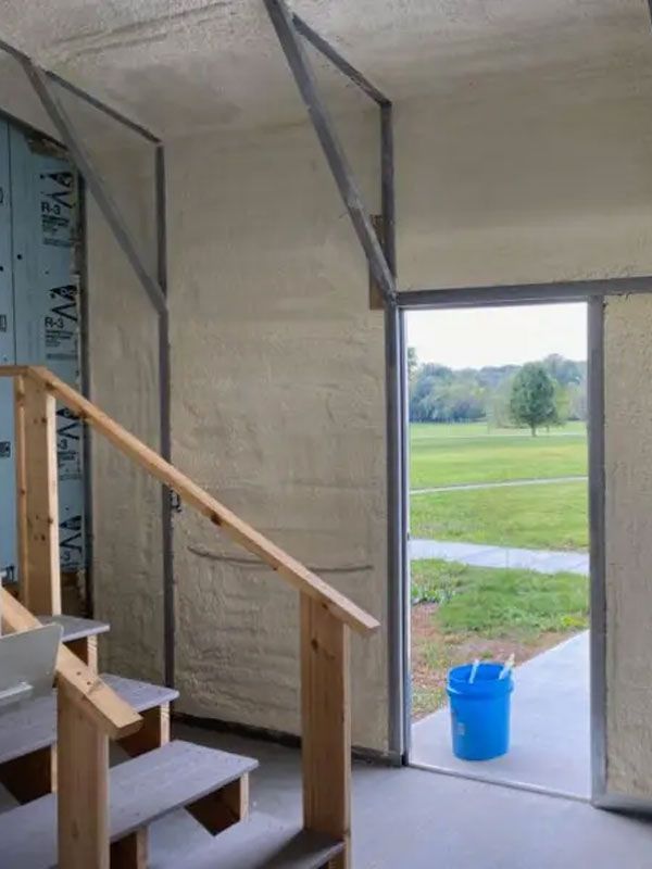 Interior stairwell opening to a grassy field, with a blue bucket by the doorway.